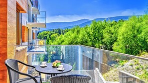 Een balkon met een tafel en stoelen, met uitzicht op een bebost gebied en bergen.