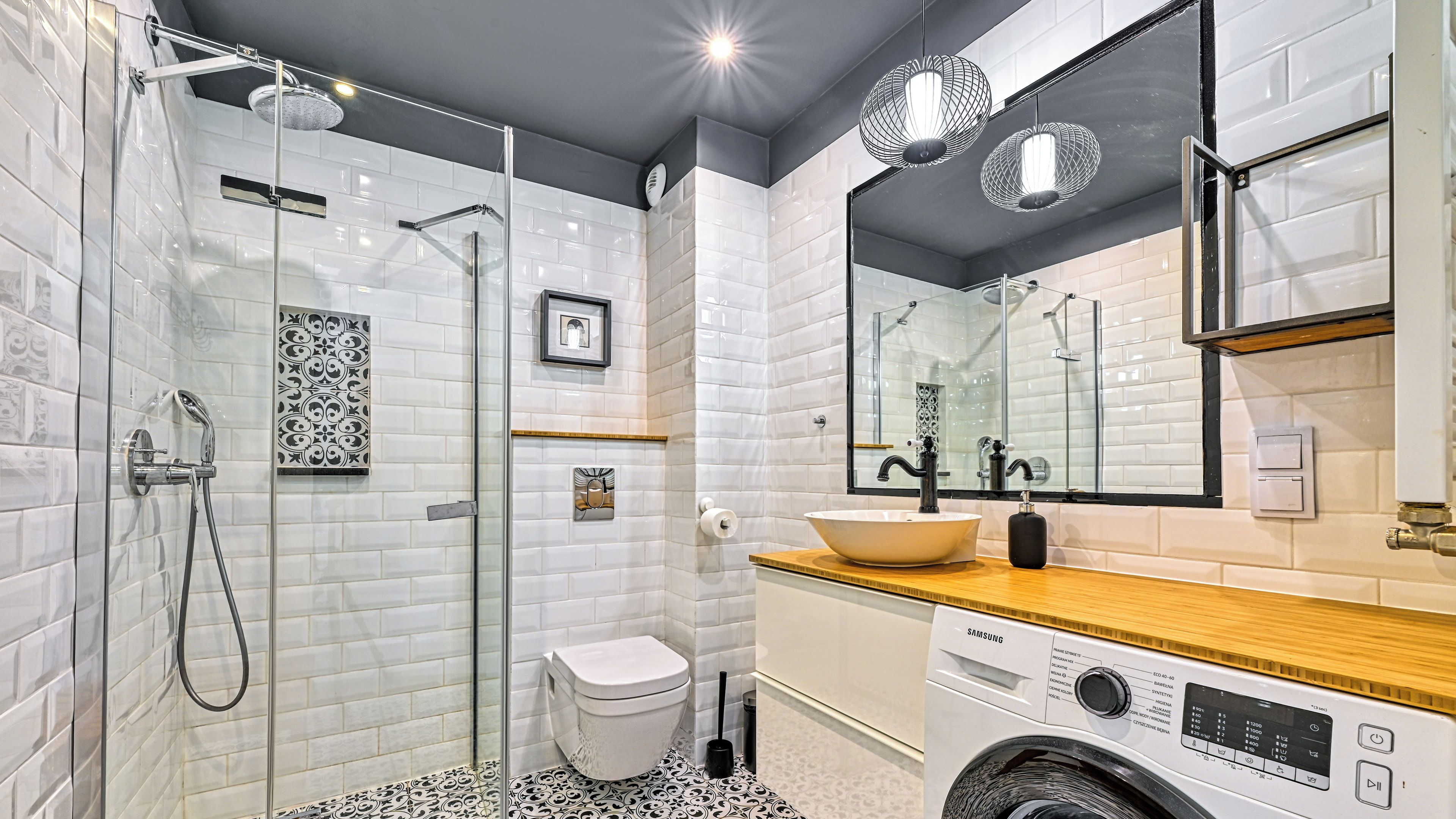 Un bany modern amb plat de dutxa envoltat de vidre, un vàter, un lavabo amb un recipient i una rentadora.