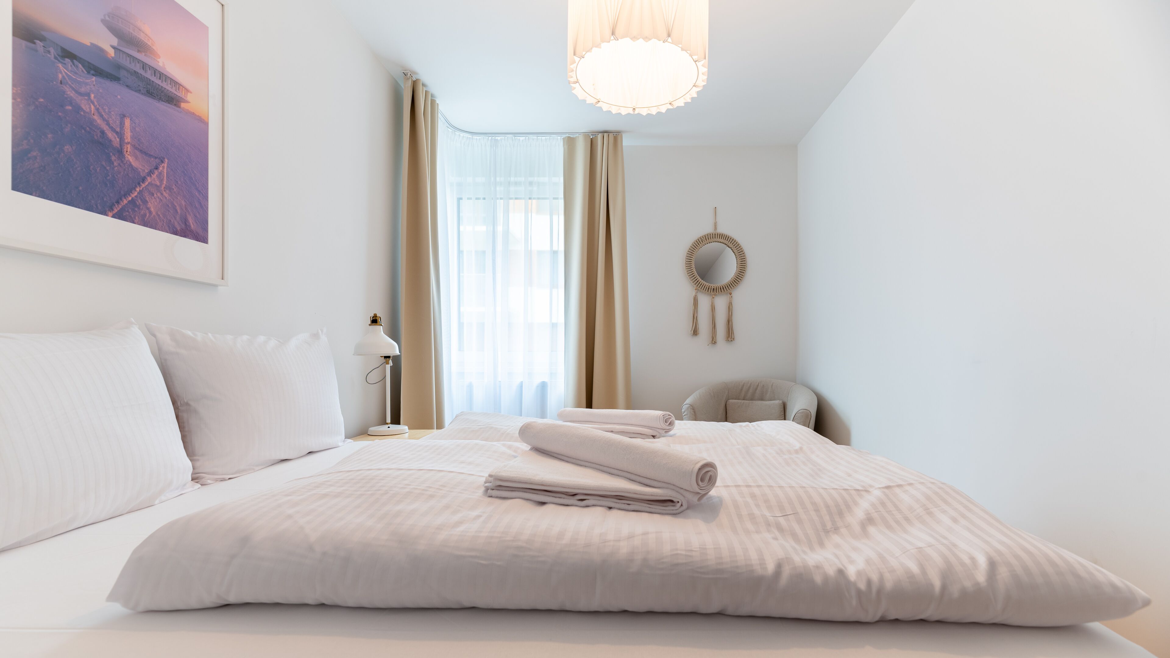 Un letto rifatto con lenzuola bianche, una lampada da comodino e uno specchio a parete.