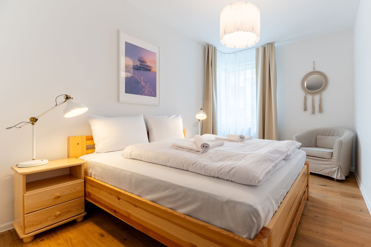 Een moderne slaapkamer met een houten bed, nachtkastjes, een bureau, een stoel, een macramé decoratie aan de muur en een lijst met een afbeelding.