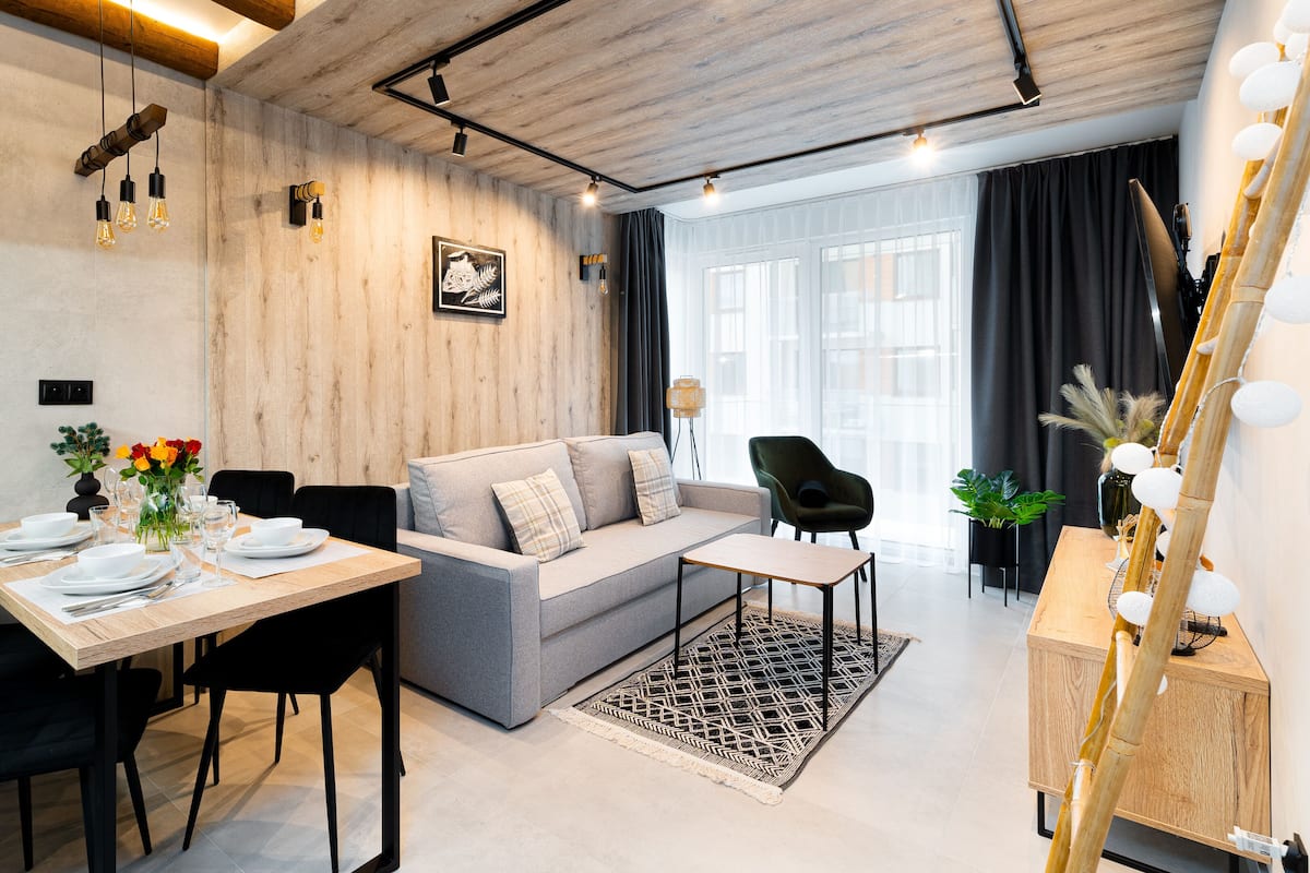 Een moderne woonkamer met een grijze bank, zwarte stoelen, een houten eettafel gedekt voor vier personen, en een salontafel.