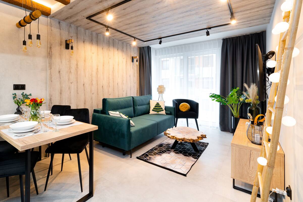 Een moderne woonkamer met een groene bank, een eettafel gedekt met borden en glazen, en een klok aan de muur.