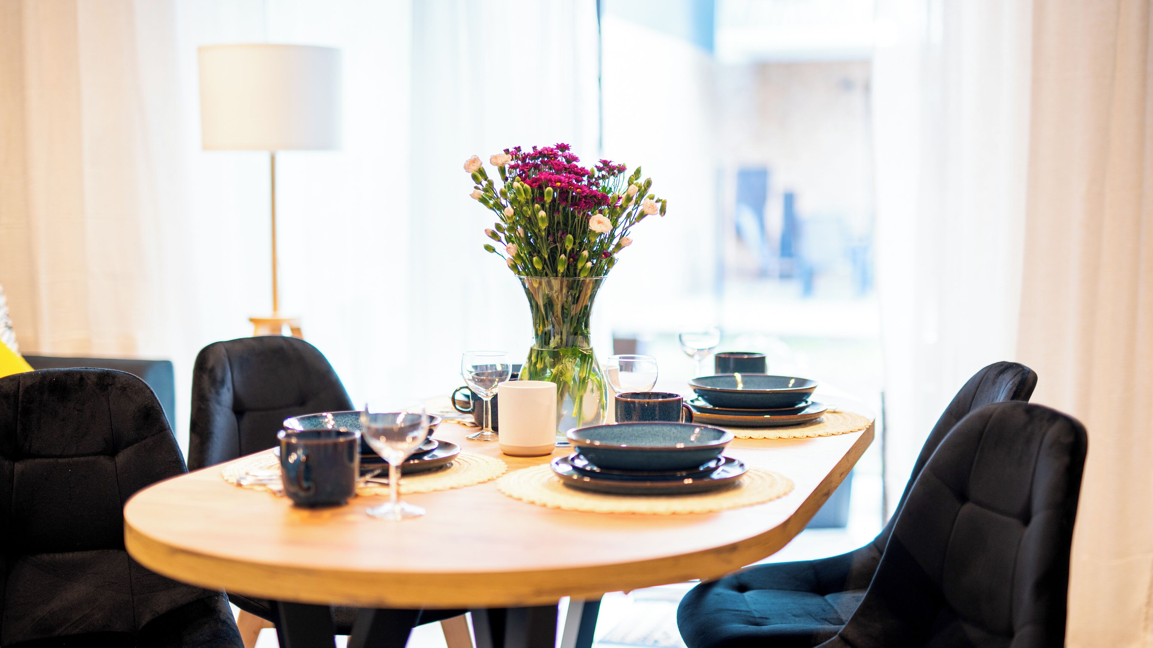 A dining table with black chairs, a vase of flowers, and various dishes and glasses.