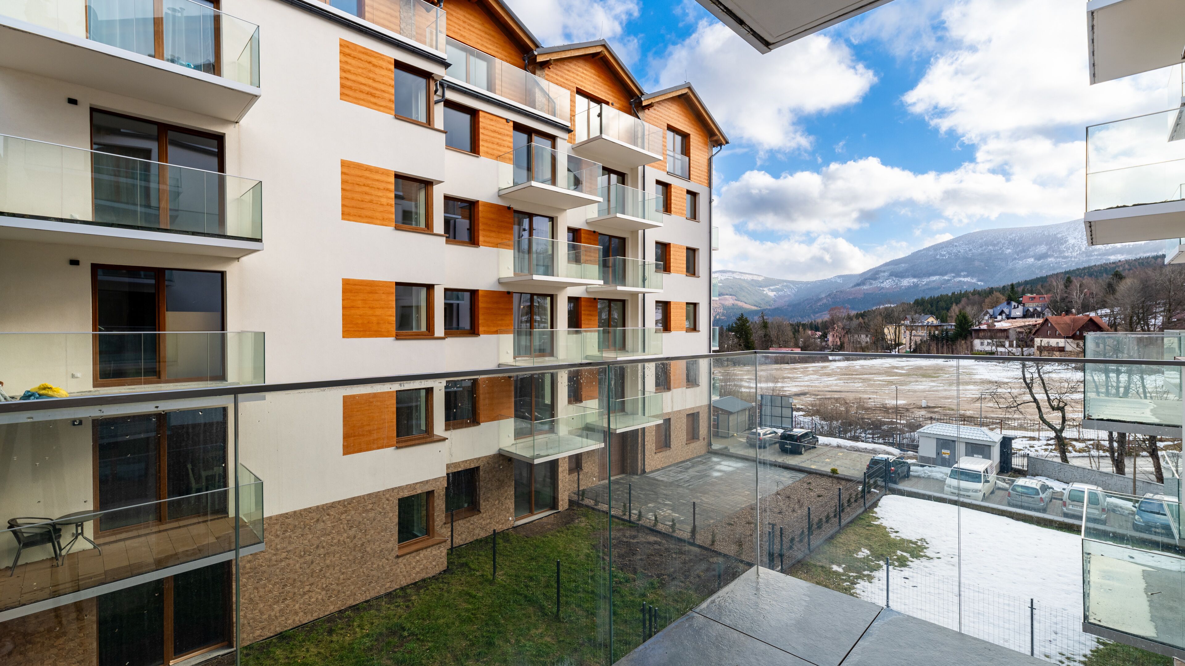 Un immeuble moderne à plusieurs étages, doté de balcons, de grandes fenêtres et offrant une vue sur un paysage enneigé avec des montagnes.