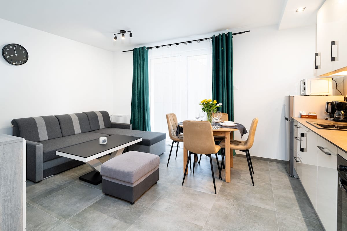 Een modern appartement met een grijze bank, een eettafel en een keuken.