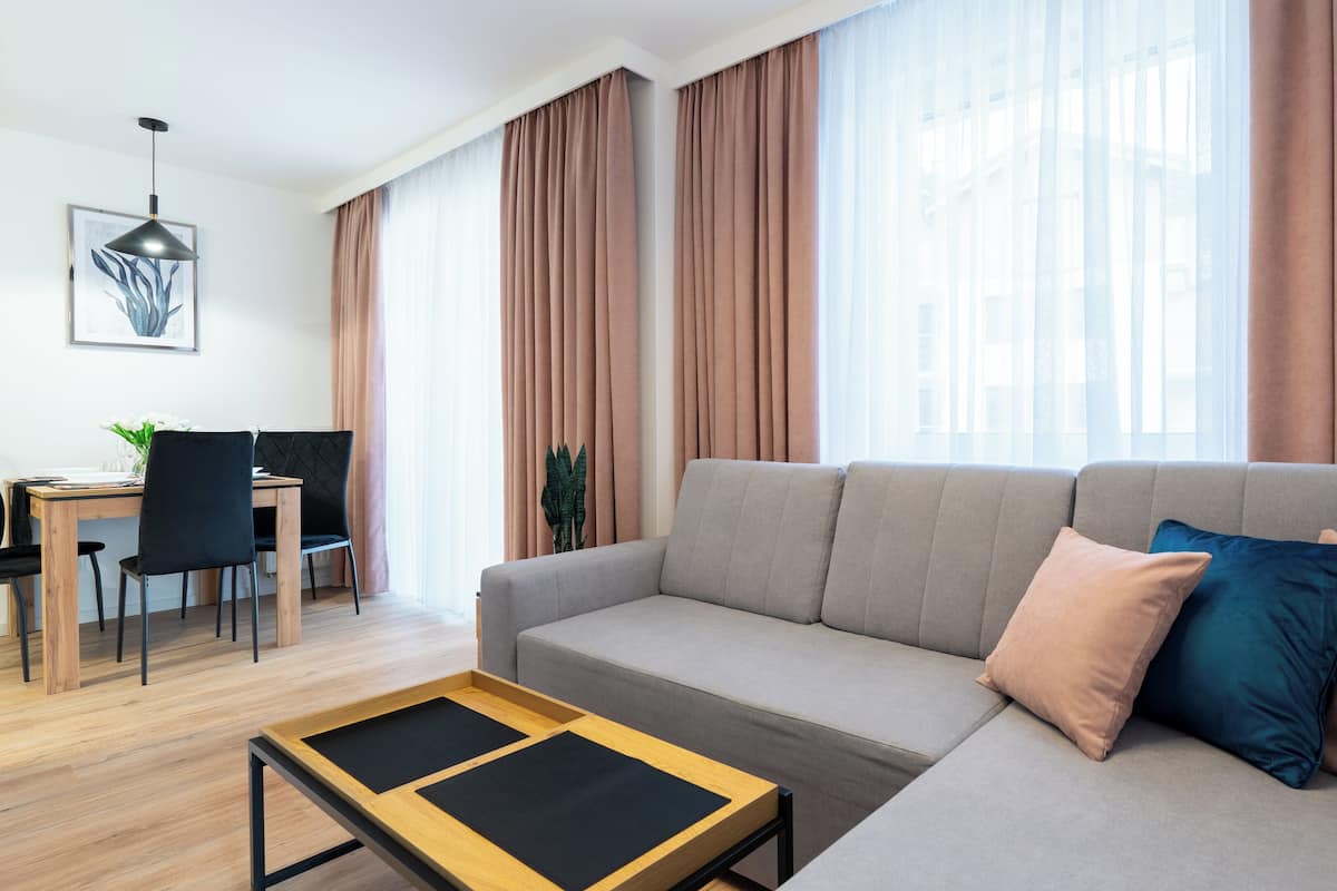 Een moderne woonkamer met een grijze bank, een houten salontafel en een eethoek met een tafel en stoelen.
