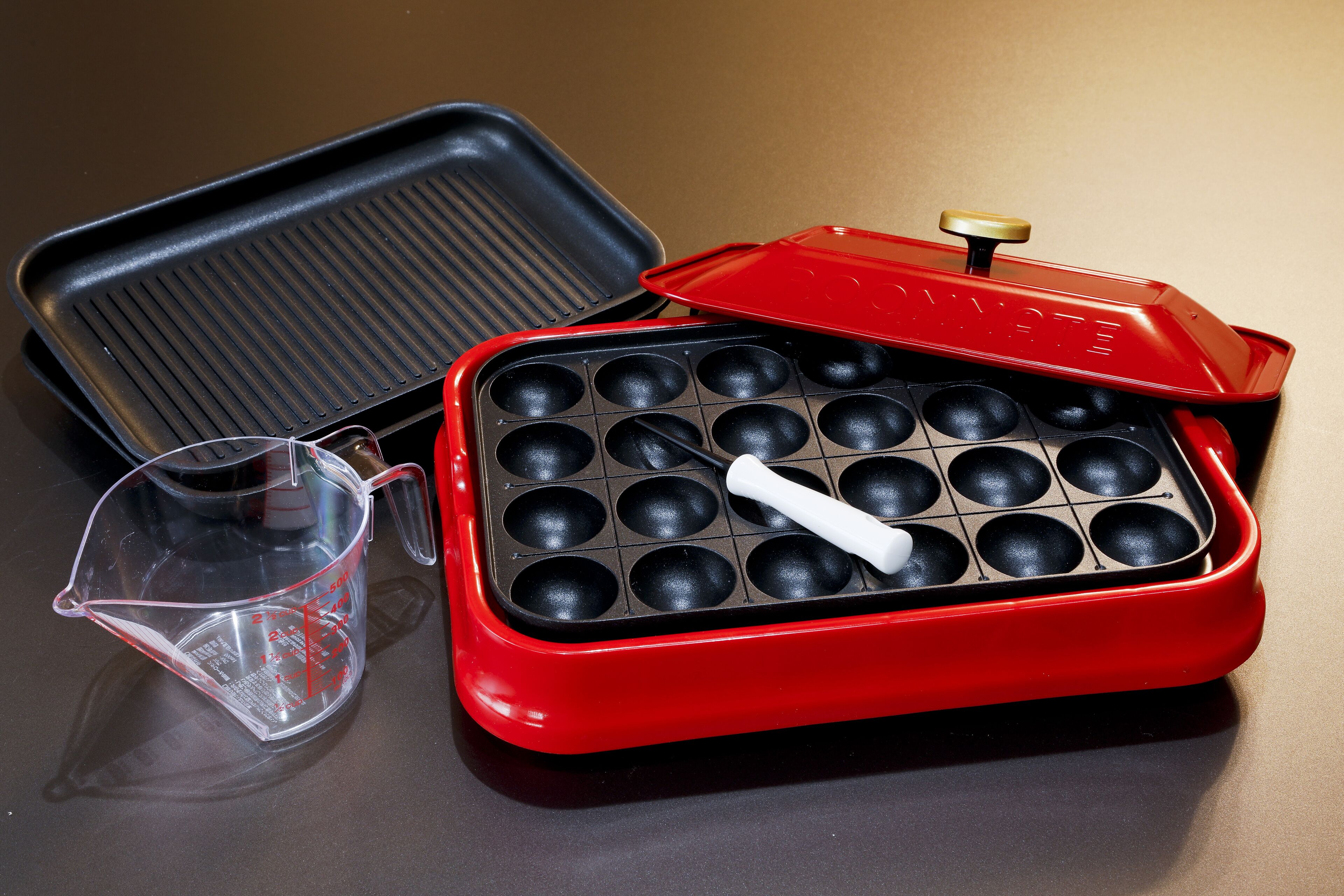 A red and black waffle iron with a measuring cup beside it.