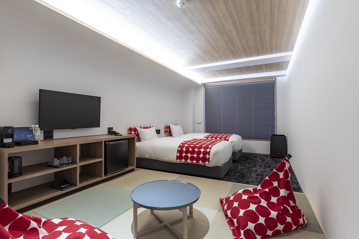 A modern hotel room with a bed, a TV, a desk, and a small table.