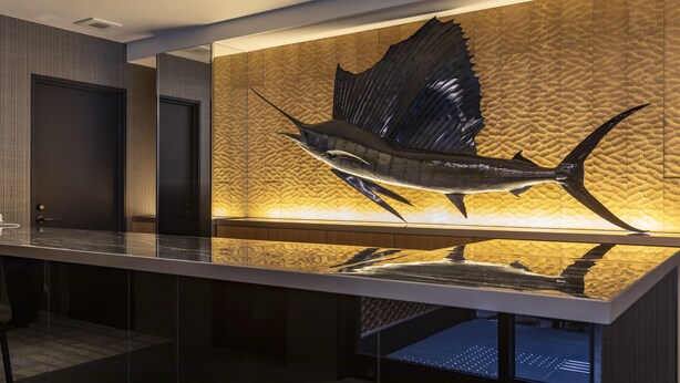 A modern interior with a large fish sculpture on a textured wall, a reflective surface below, and a door to the left.