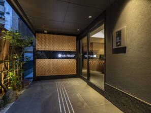 A hotel entrance with a modern design, featuring a textured wall, a signboard, and a glass door. - Tabist kiki HOTEL KYOTO Sanjo Takakura (Kyoto)