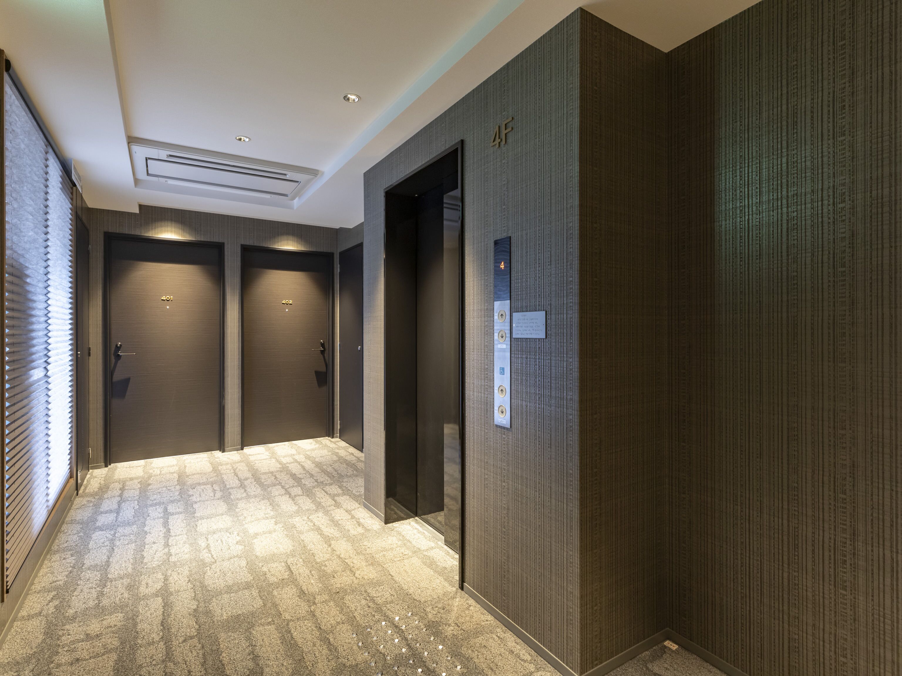 A modern hallway with two doors, an elevator, and a carpeted floor.