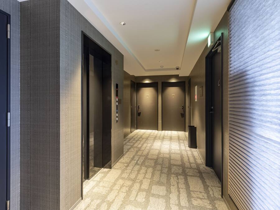 A hallway with two elevators, carpeted floor, and a door on the left.