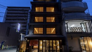 A multi-story building with a traditional Japanese architectural style, featuring a ground-level entrance with a wooden facade and a modern glass storefront on the right.