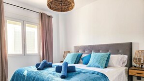 A bedroom with a large bed, a grey upholstered headboard, and a bedside table with a lamp.