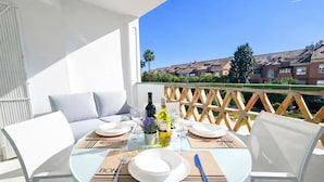 A round table set for two with white plates, cutlery, and a bottle of olive oil.