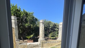 On aperçoit, à travers une porte vitrée, une cour intérieure avec une pelouse artificielle verte, des piliers en pierre et une clôture en bambou.