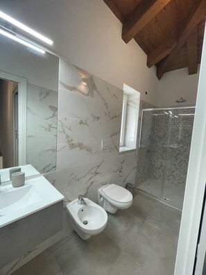 Une salle de bain moderne avec des carreaux de marbre, un bidet, des toilettes, une douche et un grand miroir.