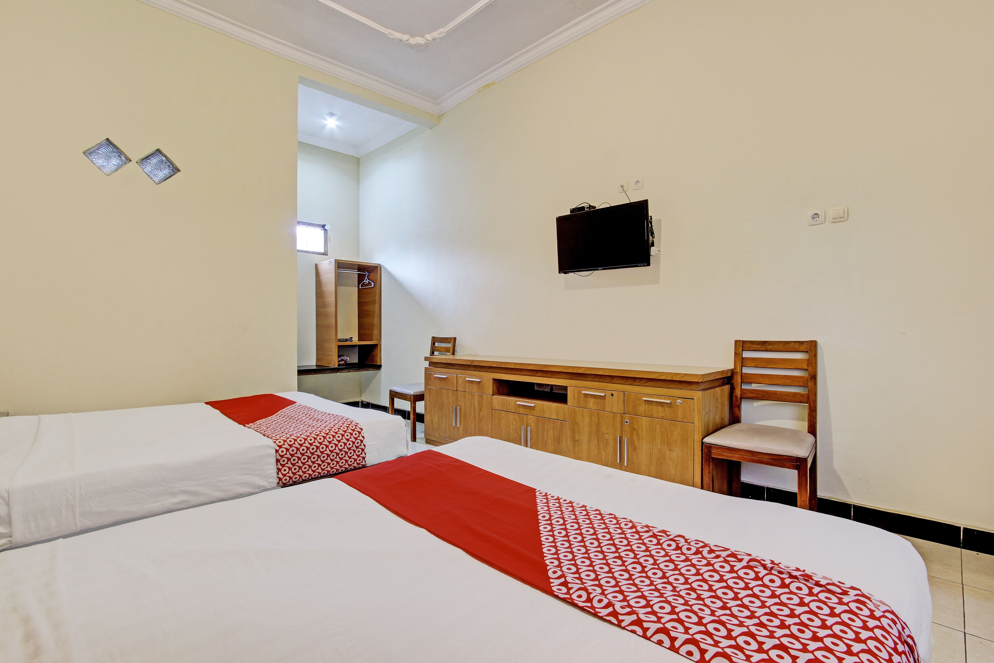 A hotel room with two beds, a wooden dresser, a chair, and a television mounted on the wall.