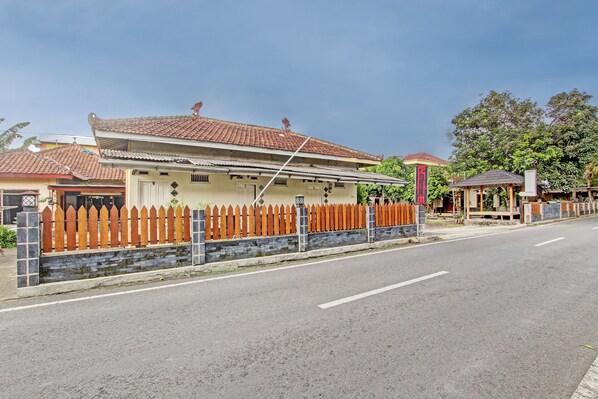 A residential street with a house featuring a tiled roof, a wooden picket fence, and a stone wall. - OYO 93660 New Family Hotel Syariah (Mungkid)