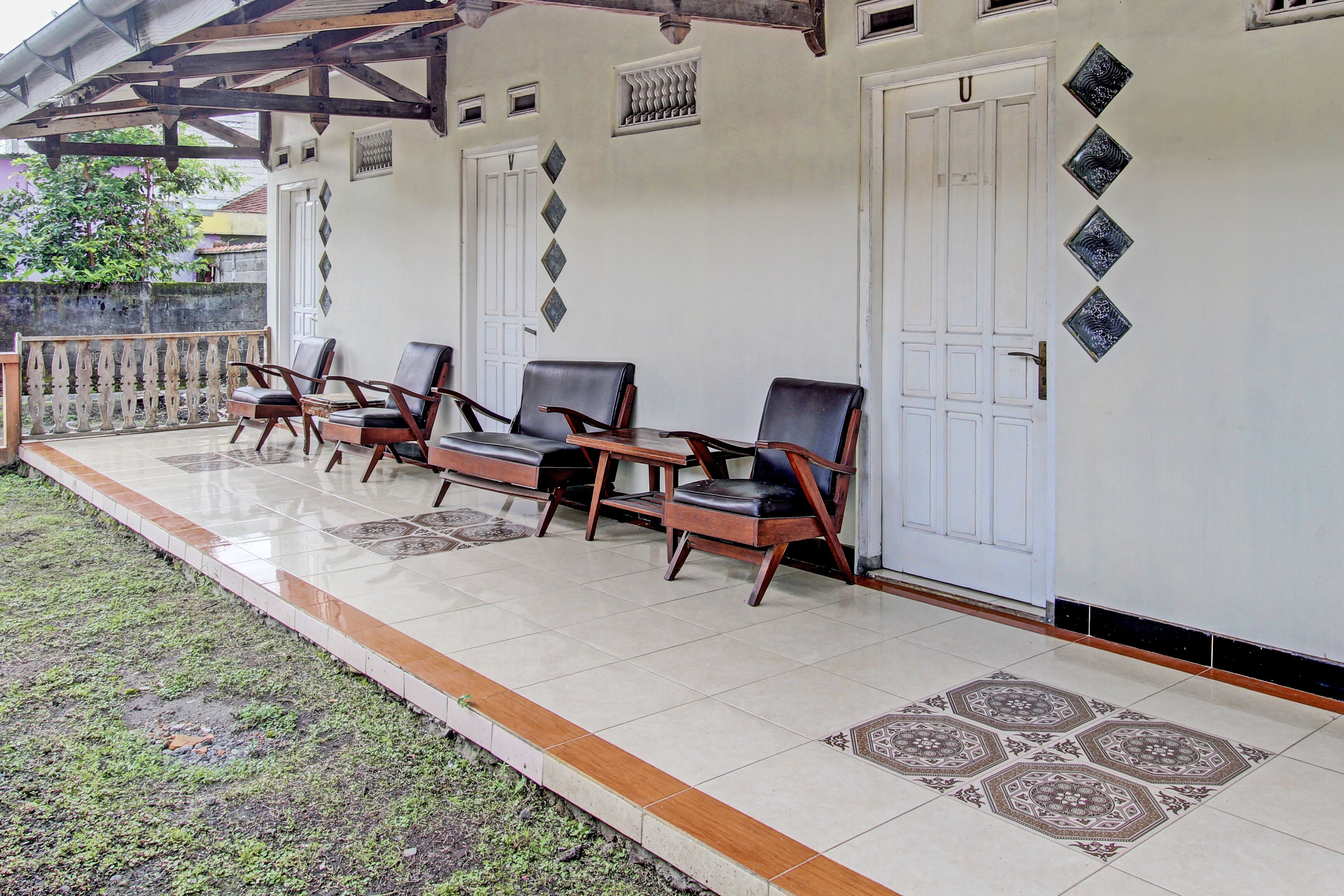 A covered outdoor seating area with four chairs and a table, a tiled floor, and a white door with decorative tiles.