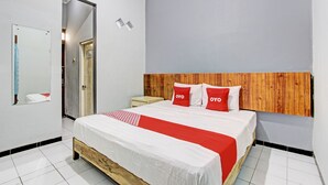 A bedroom with a wooden headboard, a bed with white and red bedding, a nightstand, and a mirror on the wall.