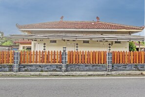A two-story building with a tiled roof, a wooden picket fence, and a stone wall. - OYO 93660 New Family Hotel Syariah (Mungkid)