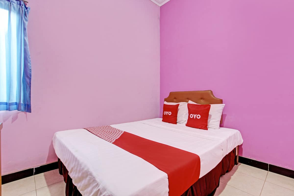 Ein Einzelzimmer mit rosa Wand, weißer Bettwäsche und roten Akzenten.