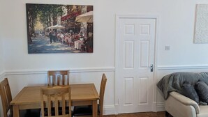 Een eetgedeelte met een houten tafel en stoelen, een witte deur en een schilderij aan de muur.