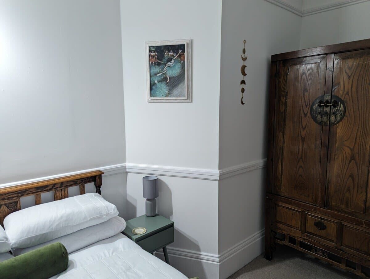 Ein Schlafzimmer mit einem Holfischschrank, einem Nachttisch mit Lampe und einem gerahmten Bild an der Wand.