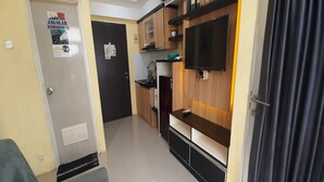 A compact kitchen with wooden cabinets, a built-in TV, and a refrigerator. - Hotel O The Jarrdin Apartment By Putra Homestay Property (Bandung)