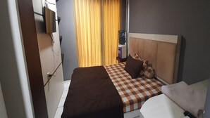 A hotel room with a checkered bedspread, a brown headboard, and a window with yellow curtains. - Hotel O The Jarrdin Apartment By Putra Homestay Property (Bandung)