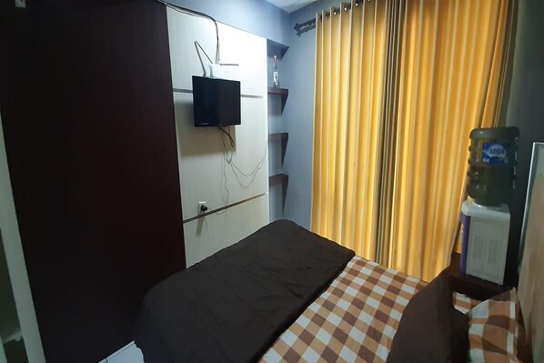 A hotel room with a bed, a television mounted on the wall, a water dispenser, and a curtain. - Hotel O The Jarrdin Apartment By Putra Homestay Property (Bandung)