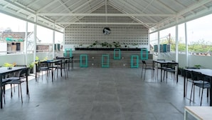 An indoor dining area with tables and chairs, a high ceiling, and a patterned wall.