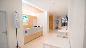 A modern reception area with a wooden reception desk, a white wall with a logo, and a seating area with tables and chairs.
