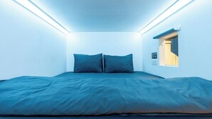 A bedroom with a bed, two pillows, a window, and a wall-mounted control panel.