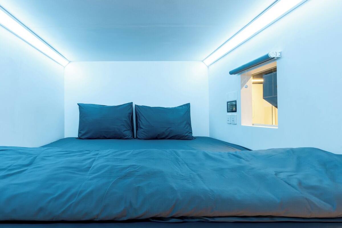 A bedroom with a bed, two pillows, a window, and a wall-mounted control panel.