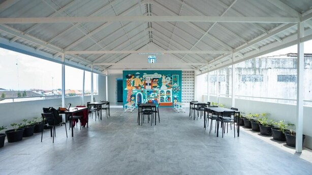 An open-plan space with a high ceiling, potted plants, and a colorful mural on the back wall.