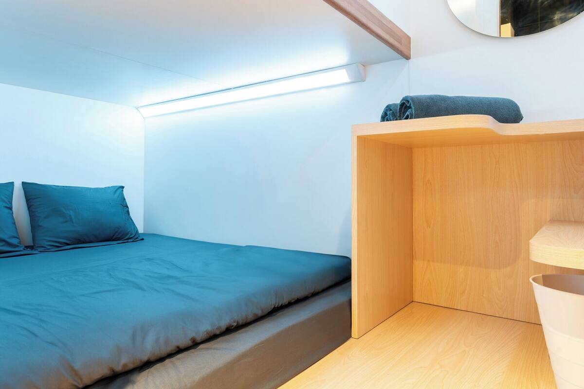 A small, modern room with a bed, a wooden shelf, and a mirror on the wall.