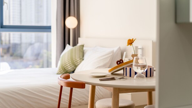 Una habitación de hotel con una cama, una mesa de comedor con un plato, un vaso y un florero con flores.