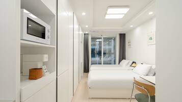 A modern hotel room with a bed, a desk, and a microwave on a built-in shelf.