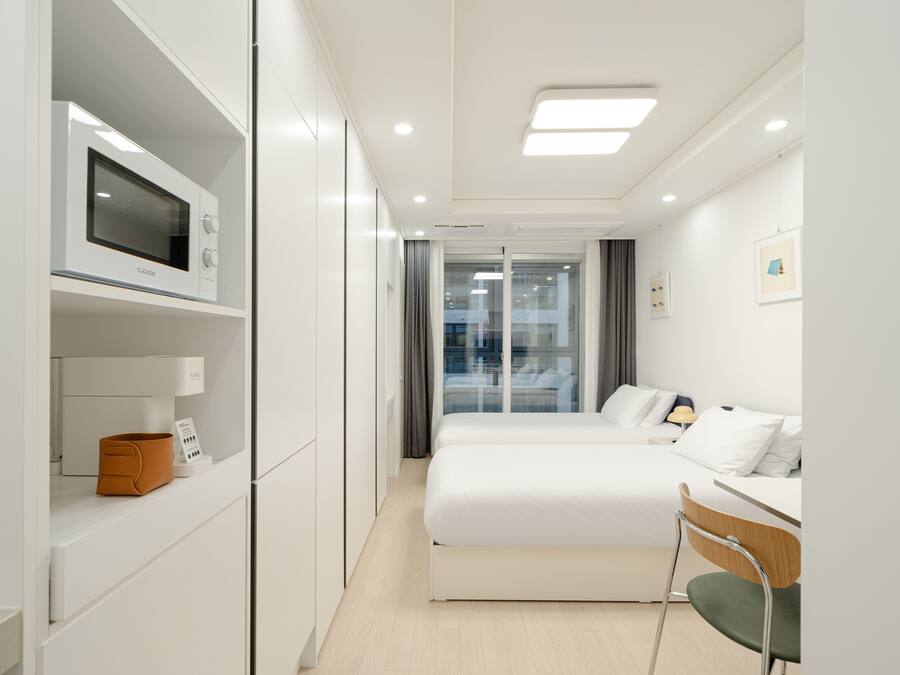 A modern hotel room with a bed, a desk, and a microwave on a built-in shelf.