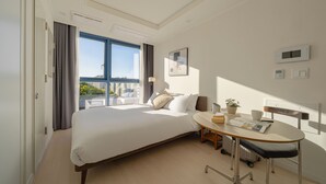 Una habitación de hotel moderna con una cama grande, una mesita redonda y vistas de la ciudad a través de un amplio ventanal.
