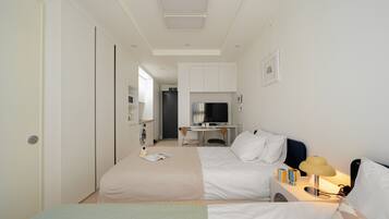 A hotel room with two beds, a desk, a TV, and a kitchenette.