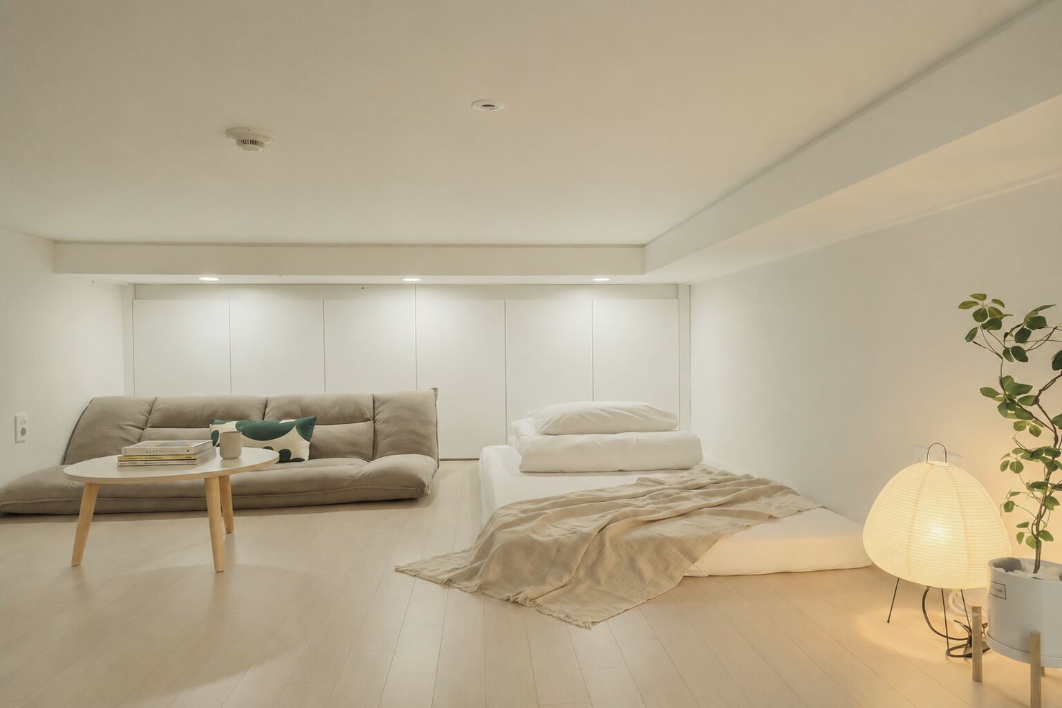 Un salón minimalista con un sofá, una mesita, una cama y una lámpara.