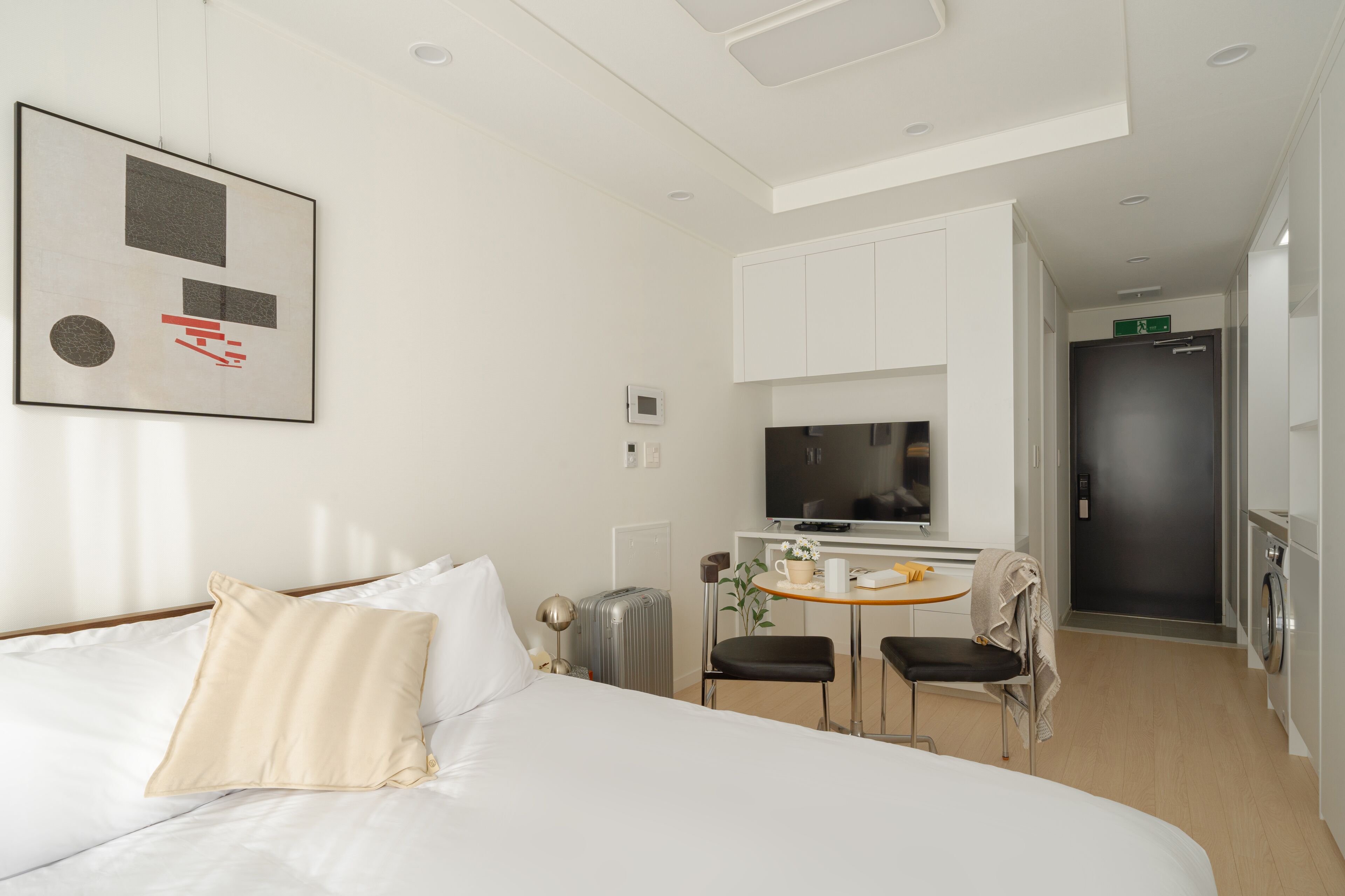 Una habitación de hotel con cama, escritorio, silla, televisor y lavadora.