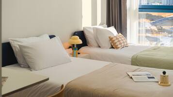 A hotel room with two beds, a desk, and a window with a view of buildings.
