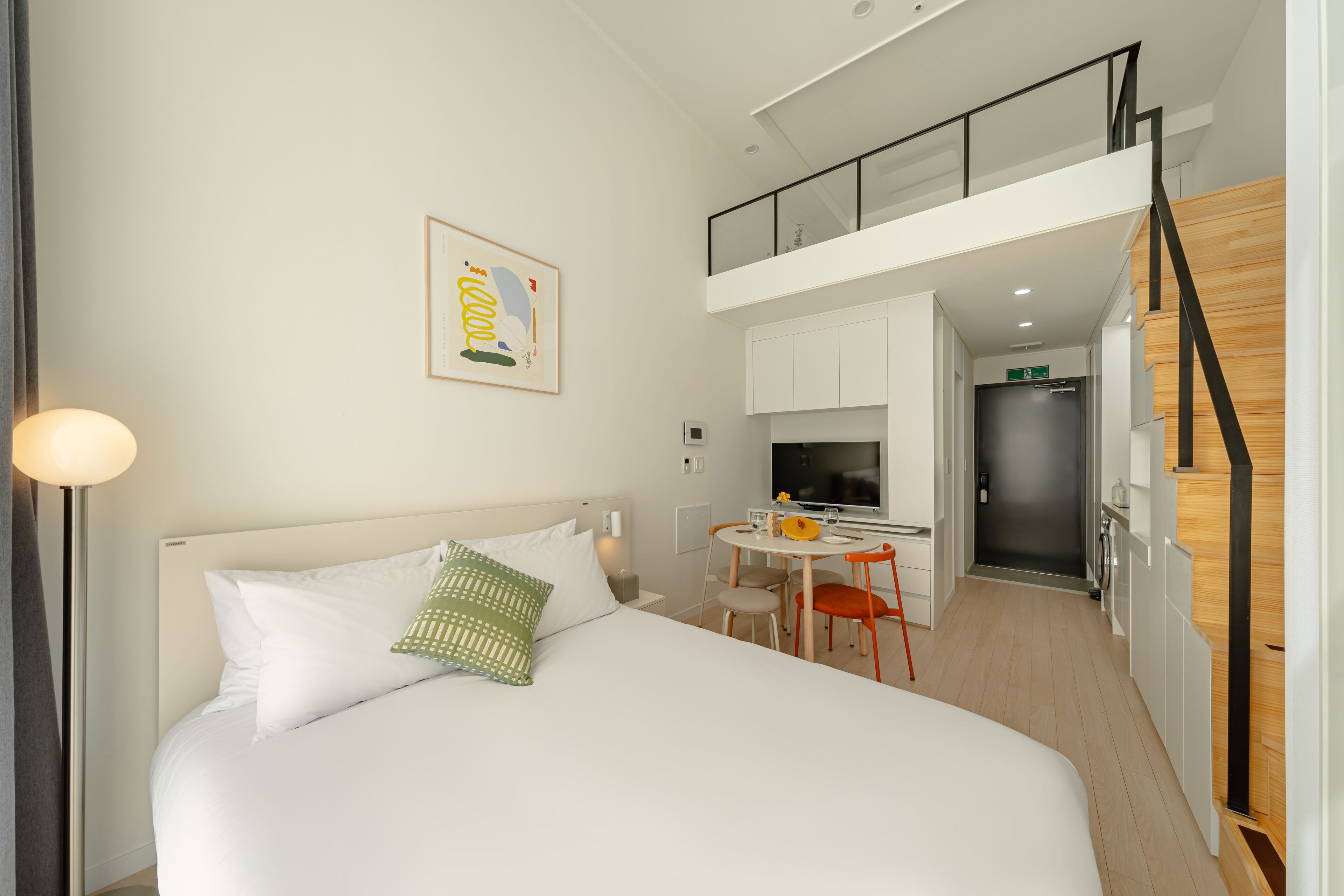 A modern hotel room with a bed, a dining table, and a kitchenette.