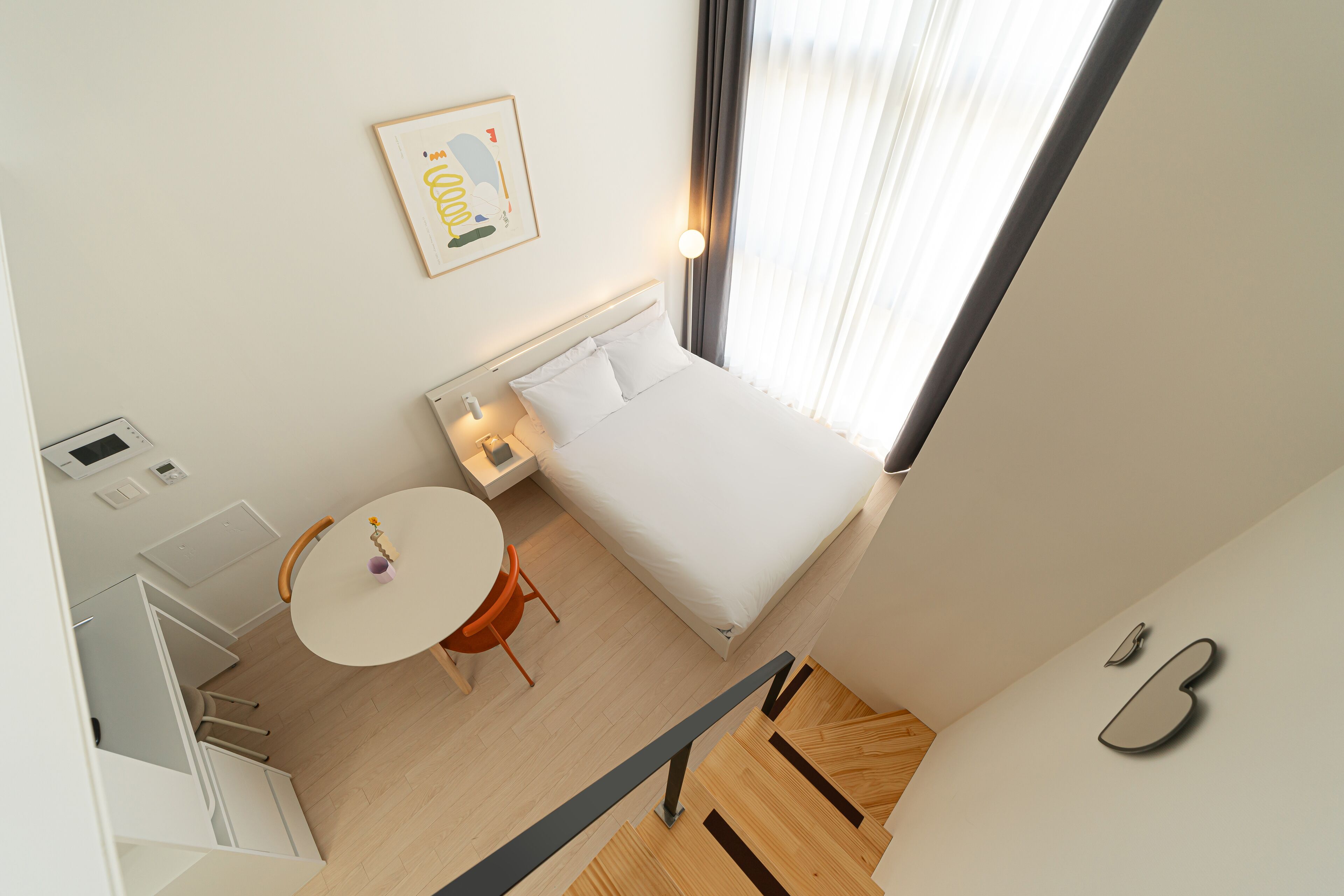 Ett modernt hotellrum med en säng, ett litet bord med en stol, ett skrivbord med en stol och ett fönster med gardiner.