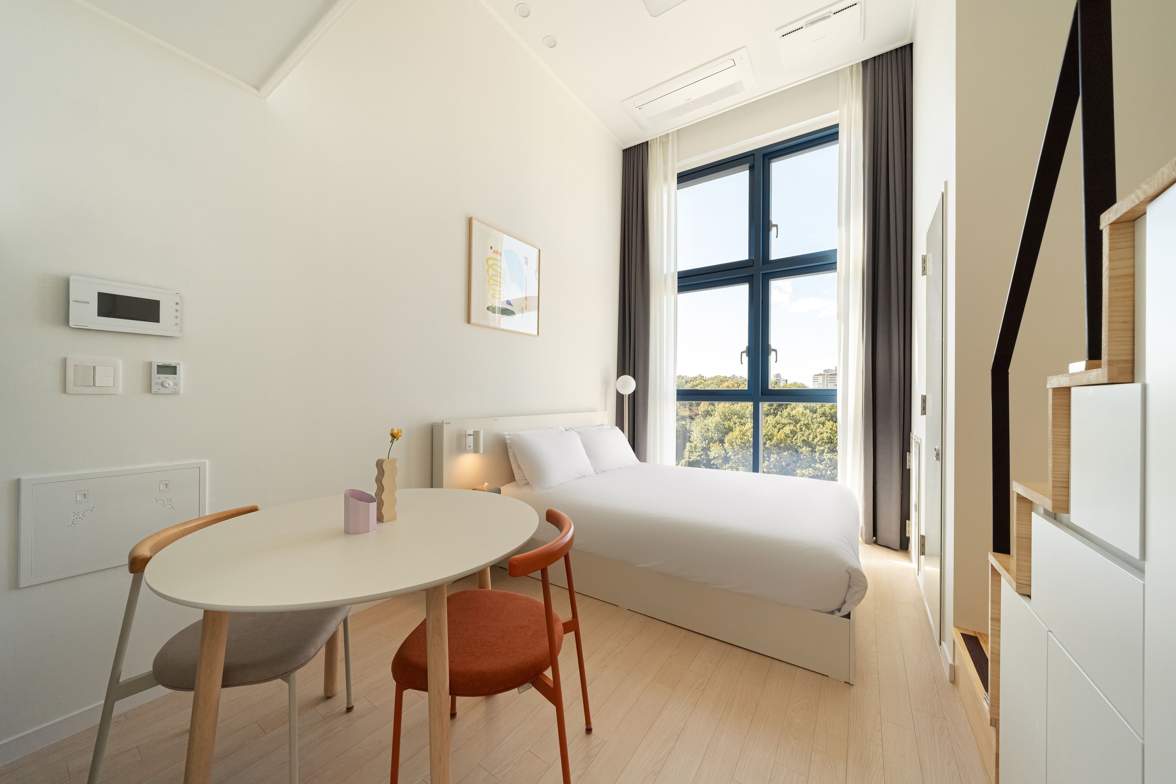 Een moderne slaapkamer met een groot raam, een bed, een nachtkastje en een stoel.