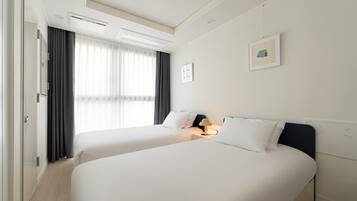 A hotel room with two beds, a window with curtains, a wall-mounted picture, and a ceiling light.